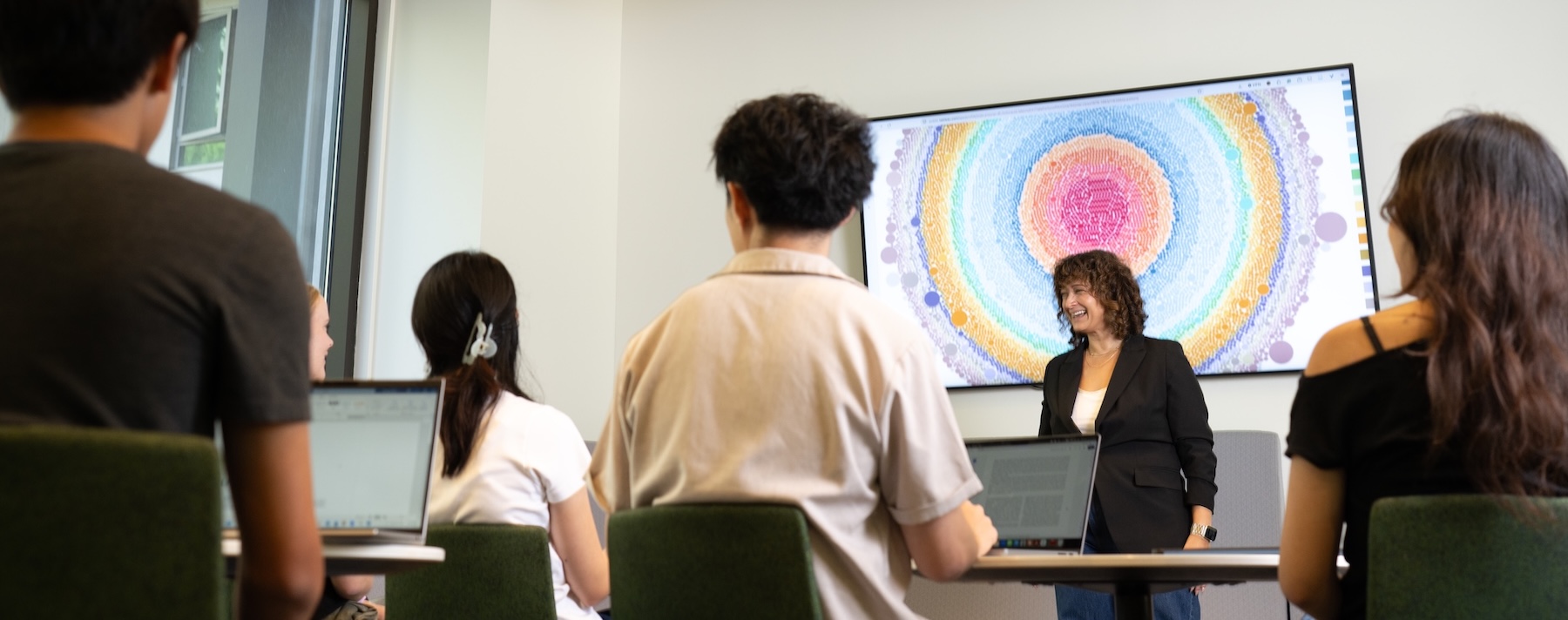Professor speaks with graduate students during a discussion of a digital research visualization.